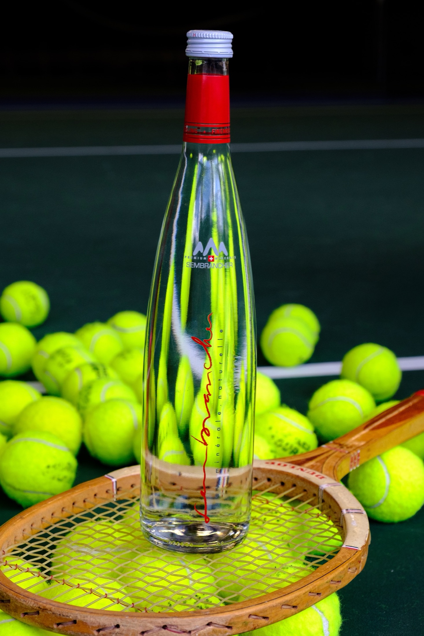 Sembrancher bottle photographed with tennis balls and a wooden tennis racquet